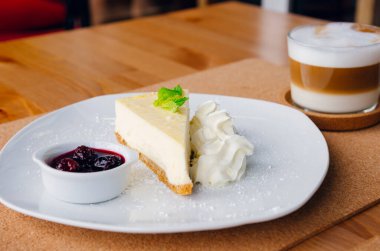 Tabakta meyve ve kapuçino olan bir dilim cheesecake.