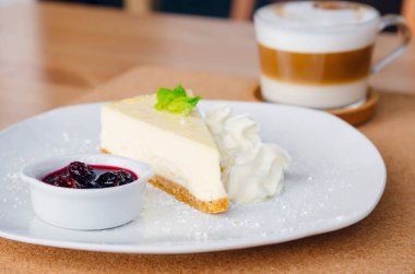 Tabakta meyve ve kapuçino olan bir dilim cheesecake.