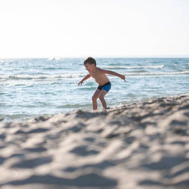 Sahilde küçük bir çocuk, yaz zamanı dalgalarla oynuyor. Rahatlama ve sağlıklı yaşam tarzı kavramı
