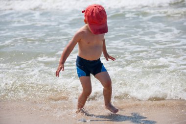 Sahilde küçük bir çocuk, yaz zamanı dalgalarla oynuyor. Rahatlama ve sağlıklı yaşam tarzı kavramı