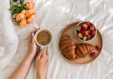 Bir fincan kahve beyaz çarşaf ile yatağa holding Womans eller.