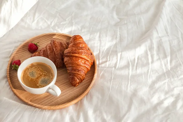 Café y croissants en la ropa de cama blanca en la habitación llena de luz solar . — Foto de Stock