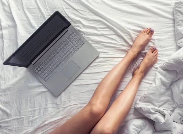 Womans legs on the bed and laptop standing near.