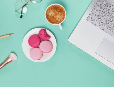 Dizüstü bilgisayar, kahve ve diğer aksesuarları pastel yeşil arka planda, üstten görünüm.