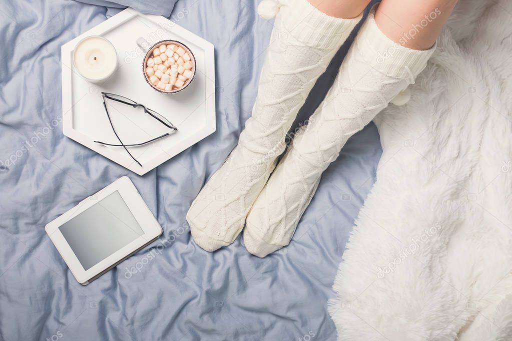 Womans legs in socks and cup of cocoa with marshmallows.