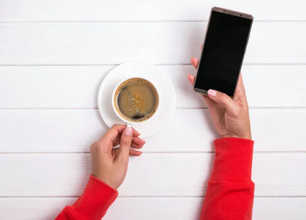 Γυναικεία χέρια με το κόκκινο ρούχο κρατώντας smartphone και καφέ — Φωτογραφία Αρχείου