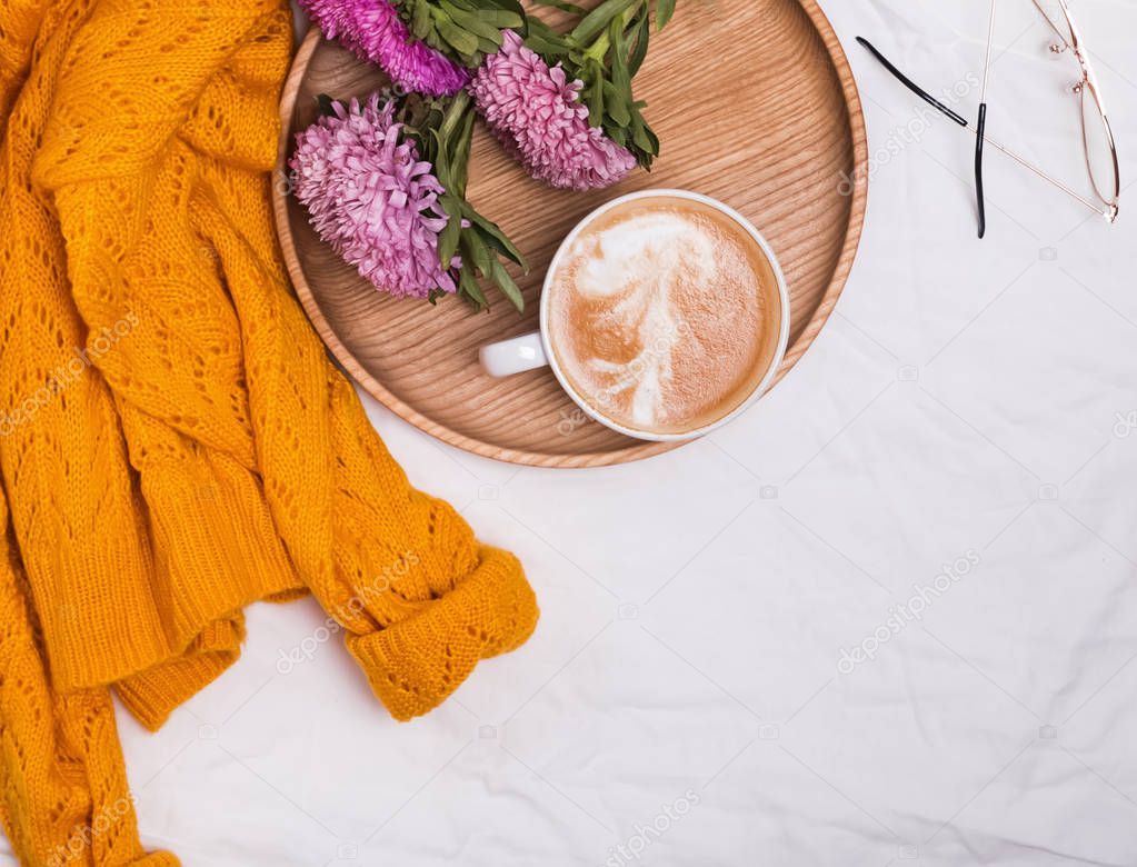 Coffee on wooden tray, flowers and yellow knitted sweater