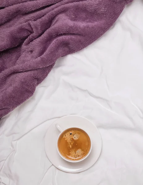 一杯咖啡在床上与白色床单和紫色毯子 — 图库照片