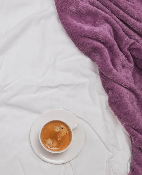 Kopp kaffe på sängen med vita lakan och lila filt — Stockfoto