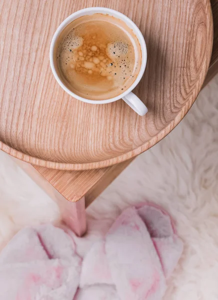 Kaffe på den träbricka står på det lilla bordet och rosa tofflor på golvet. — Stockfoto