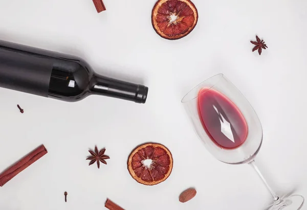 Bottiglia di vino, bicchiere con vino versato e spezie secche sullo sfondo bianco — Foto Stock