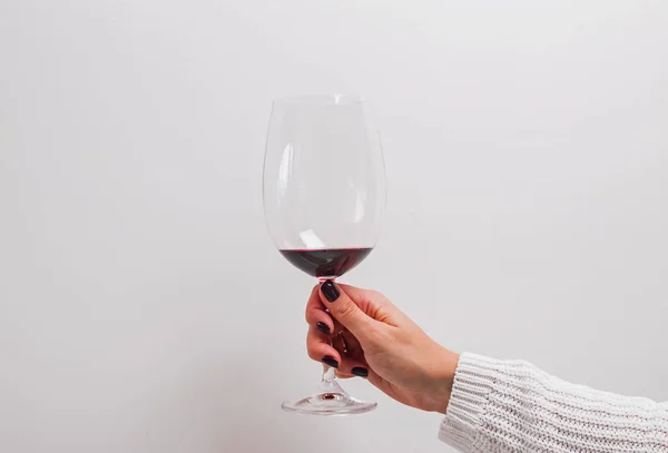 Mão das mulheres em uma camisola branca segurando um copo de vinho tinto . — Fotografia de Stock