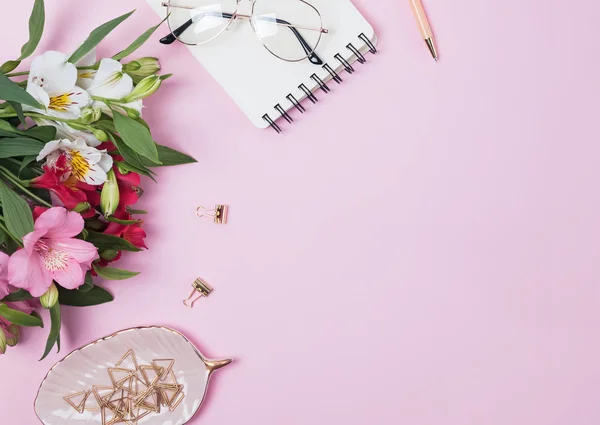 Flowers, notepad and stationery on pink background.