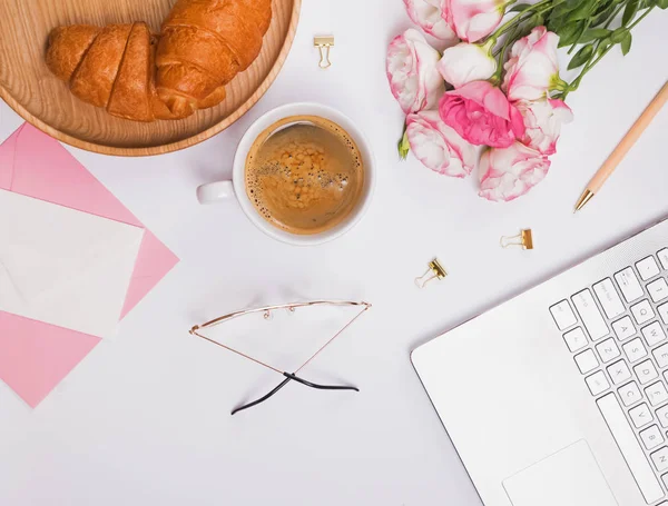 Coffee, croissants on the tray, flowers and small accessories on the white table, top view.