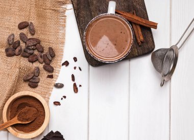 Kupası, kakao çekirdekleri ve toz beyaz tahta masada sıcak çikolata