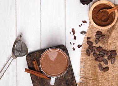 Kupası, kakao çekirdekleri ve toz beyaz tahta masada sıcak çikolata