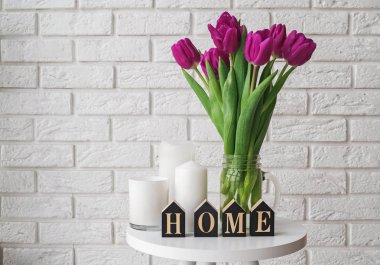 Cam bir kavanozda mor laleler ve bir kelimeye dizilmiş ahşap harfler.