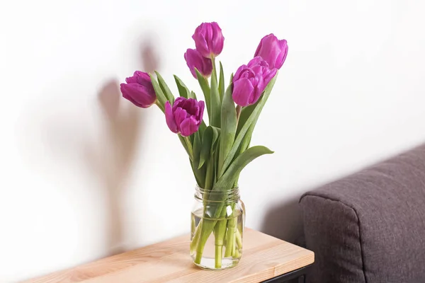Fialové tulipány v sklenice stojící na dřevěný stůl — Stock fotografie