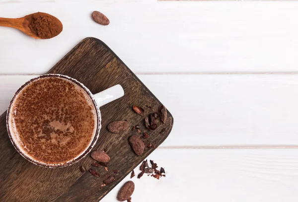 Chocolate quente na xícara, grãos de cacau e pó na mesa de madeira branca — Fotografia de Stock
