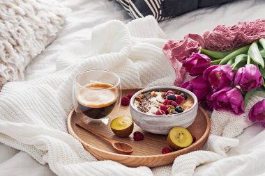 Arka plan beyaz yatakta güler yüzlü kase ve mor laleler