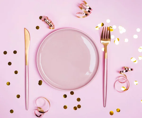 Różowy talerz, widelec i nóż oraz złote connfetti i wstążki na różowym tle, — Zdjęcie stockowe