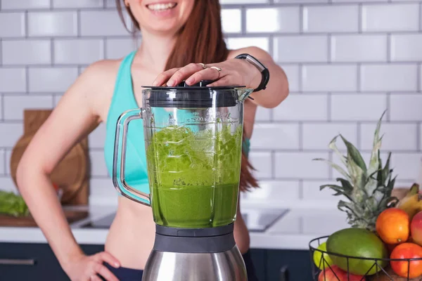 Woman making green smoothie on the kitchen.