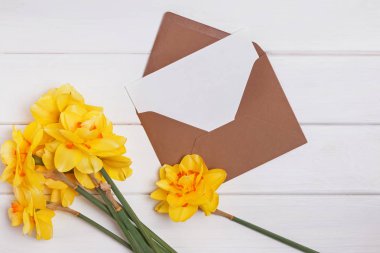Zarfta boş kağıt ve beyaz ahşap masada sarı bahar çiçekleri