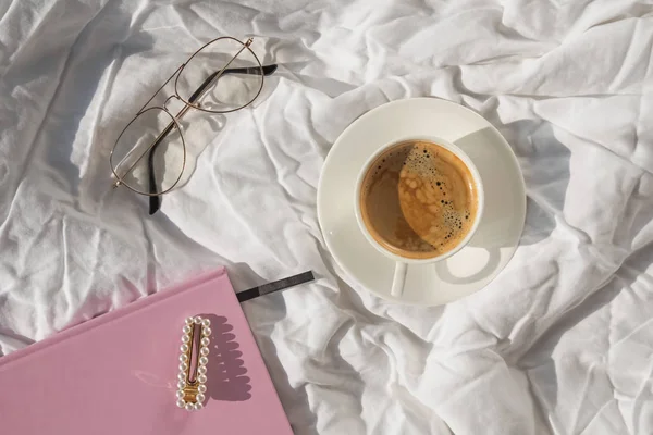 Matin plat étendu avec café, bloc-notes et lunettes sur le lit blanc — Photo