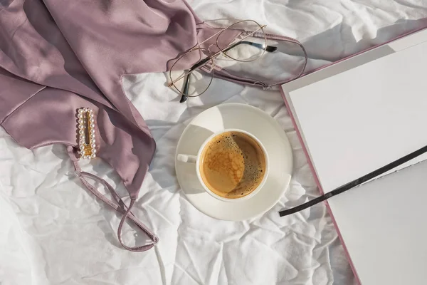 Feminint tillbehör, topp och kaffe på den vita sängen — Stockfoto