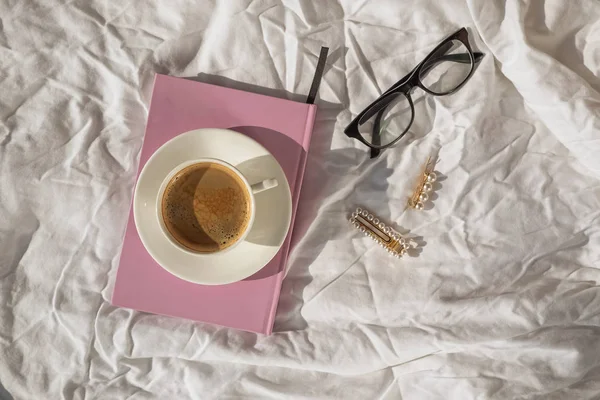 Morning flat lay with coffee, notepad and glasses on the white bed