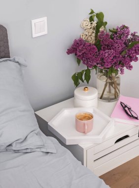 Yatağın yanındaki komidede duran kahve ve çiçekler.