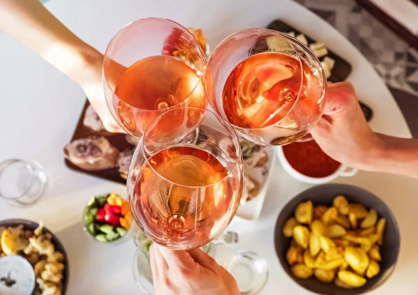 Mãos segurando copos com vinho rosa sobre a mesa com comida . — Fotografia de Stock