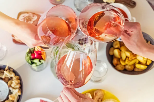 Mãos segurando copos com vinho rosa sobre a mesa com comida . — Fotografia de Stock