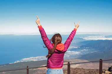 Pembe ceketli genç kadın bakış açısıyla elleri gökyüzüne kaldırarak ayakta duruyor