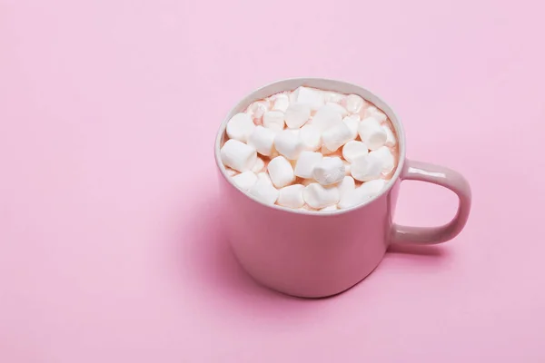 A cup of hot cocoa with a lot of marshmallows on the pink background