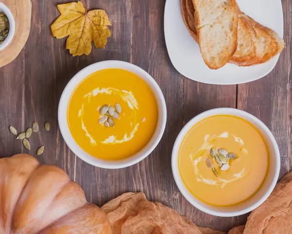 Duas taças de sopa de abóbora caseira deliciosa com creme na vista superior da mesa de madeira — Fotografia de Stock