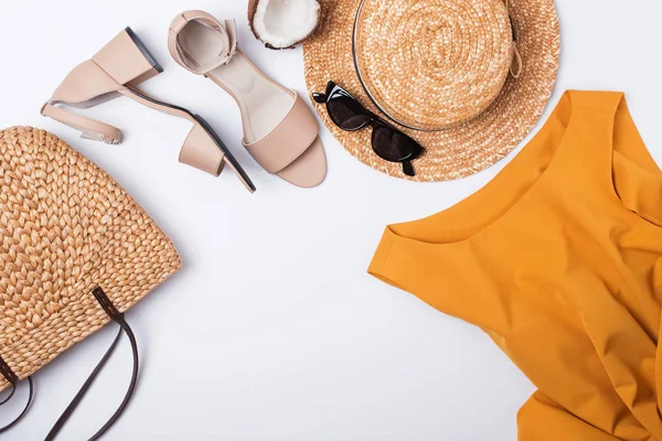 Feminine stylish summer outfit with sandals, straw hat and bag on the white table,