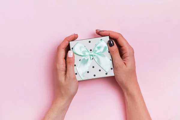 Wonans handen met mooie manicure houden giftbox op roze achtergrond — Stockfoto