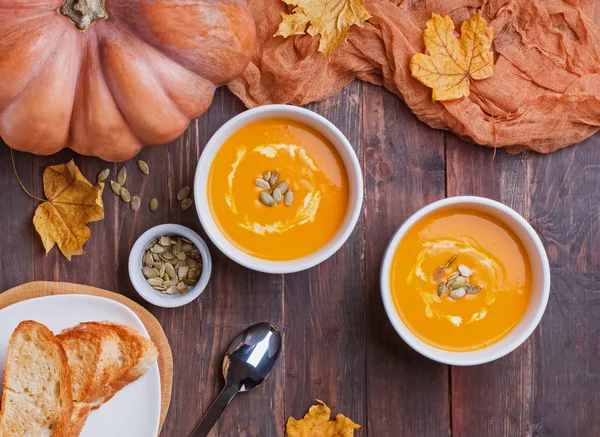 Two bowls of delecious homemade pumpkin soup with cream on the wooden table — Stock Photo, Image