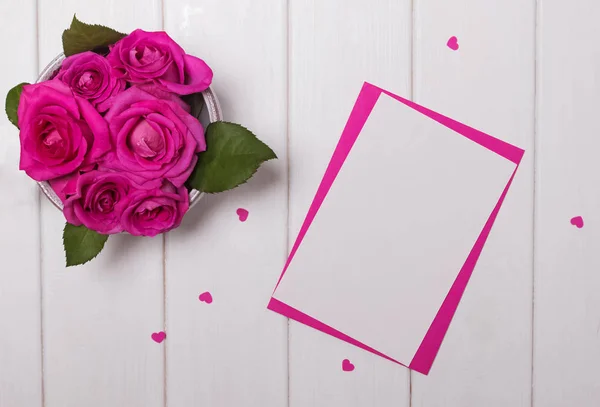 Maquette avec roses roses et petits coeurs en papier sur la table en bois blanc, vue de dessus — Photo