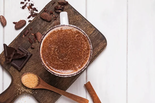Cioccolata calda nella tazza, fagioli di cacao e polvere sul tavolo di legno bianco — Foto Stock