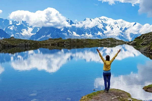 Jovem mulher de pé na costa do lago de montanha cênica em Alpes com as mãos levantadas . — Fotografia de Stock