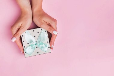 Açık pastel pembe arka plan üzerinde giftbox tutan kadın elleri,
