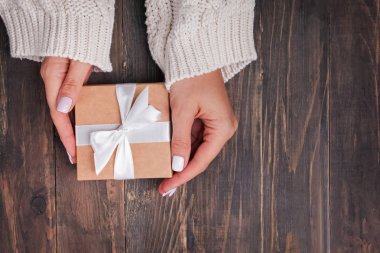 Ahşap arka plan üzerinde bir hediye kutusu tutan örme kazak kadın elleri