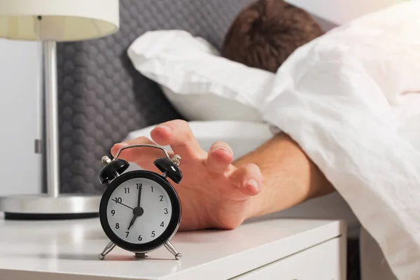 Mans hand reaching out alarm clock on the nightstand early in the morning.