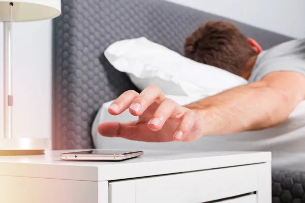 Mans hand close-up trying to reach out ringing cell phone or alarm to have some snooze