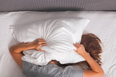 Yatakta yatan ve başını yastıkla kaplayan kadın.