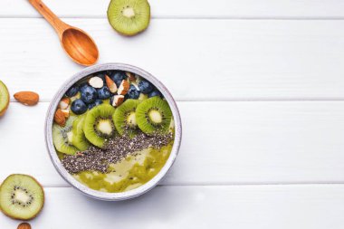 Beyaz masada dilimlenmiş kivi, chia tohumu ve yaban mersini ile süslenmiş lezzetli smoothie kase