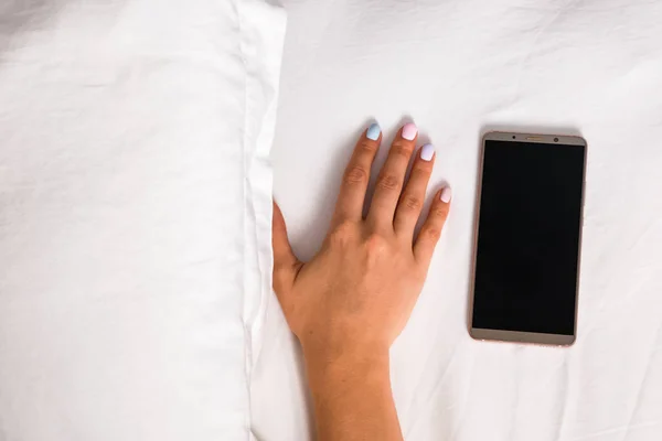 Las manos de las mujeres que yacen cerca del smartphone en la cama —  Fotos de Stock
