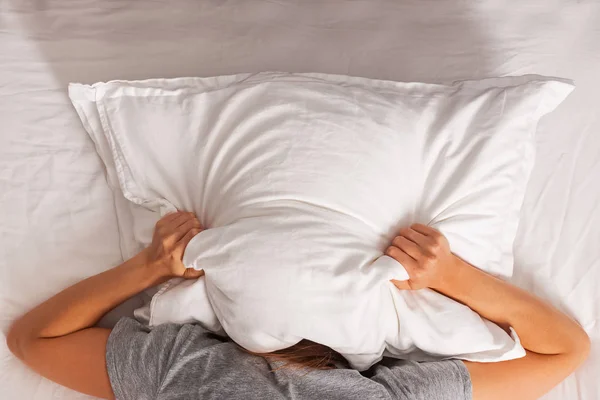 Donna sdraiata a letto e che si copre la testa con un cuscino . — Foto Stock